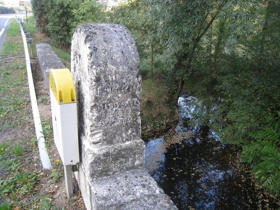Plaque de plastique vulgaire bêtement installée devant une jolie borne en pierre