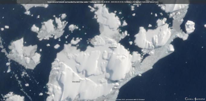 White, snow covered islands, glued together with thinner sea ice are surrounded by dark bue sea, dotted with icebergs
