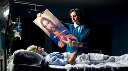 Una mujer muestra una imagen de Jesús con una frase que reza "Jesús te ama" a una niña postrada en una cama de hospital.