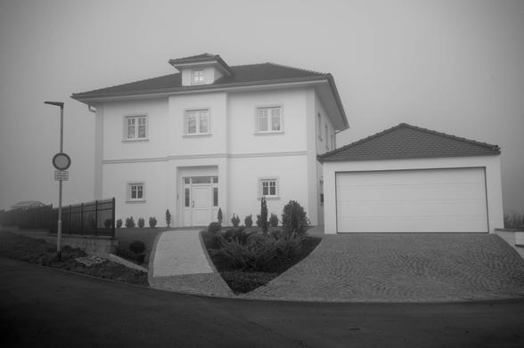 Modernes 1-Familen Häuschen mit viel zu großer, freistehender, Garage vor dichtem Nebelhintergrund.