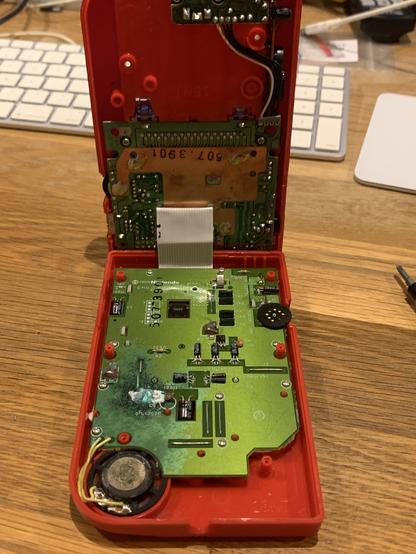 Red original GameBoy opened up showing a large PCB with corrosion and a smaller PCB.