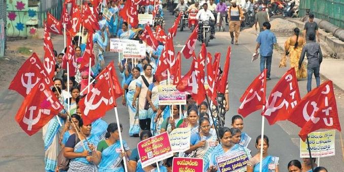 A crowd of women holding hammer and sickle flags march down a street
