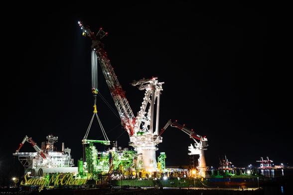 Large ship-mounted crane lit up and working at night.