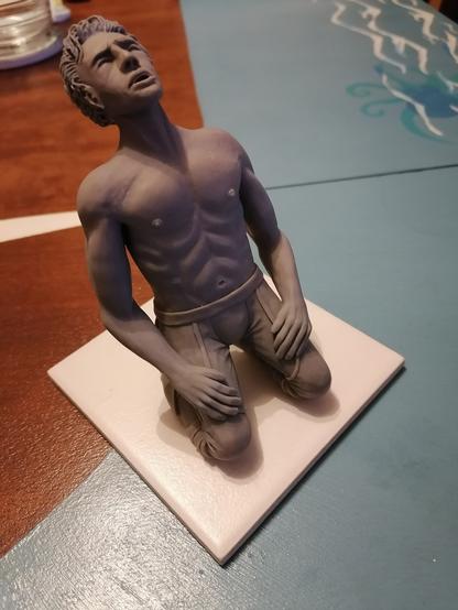 Eine graue Figur aus Skulpey die verzweifelt auf dem Boden kniet, die Hände im Schoß, den Kopf nach oben geneigt mit weinend offenem Mund und geschlossenen Augen. Es ist Astarion aus dem Spiel Baldurs Gate 3 bei einer seiner bewegensten Szenen aus dem Spiel.