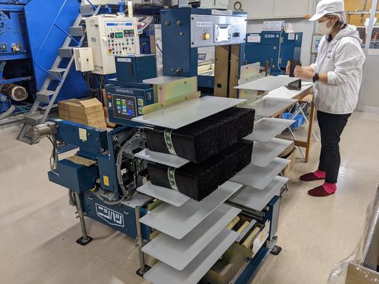 Bundles of nori sheets on shelves next to a machine on a factory floor