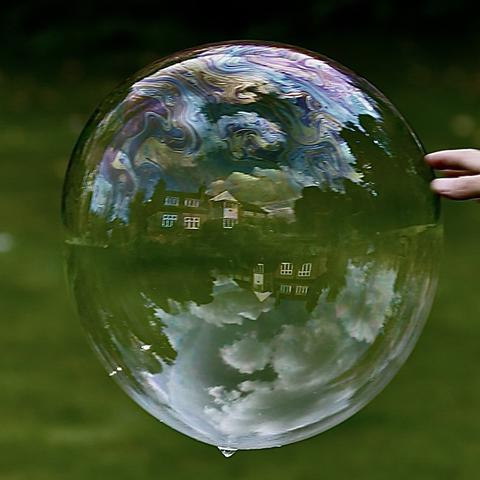 A giant soap bubble reflecting colourful clouds, buildings, grass etc.
On the right side of the bubble a small hand is trying to touch the bubble and hence burst it.
It did work :-)
