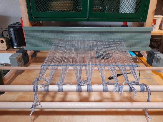 fixé à une  table par deux serre-joints hors-champs, un métier à tisser est endilé sde laine grise chinée. le fil est juste tendu et noué, le travail attend d'être commencé