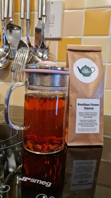 Glass teapot with an infusion of tea leaves alongside a packet of loose tea.