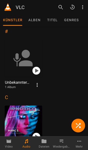 Screenshot aus der VLC App für Android. Der Reiter Musik ist geöffnet und es können die Rubriken "Künstler, Alben, Titel, Genres" ausgewählt werde. Oben links ist das Logo von VLC eingeblendet. Eine Warnpylone.