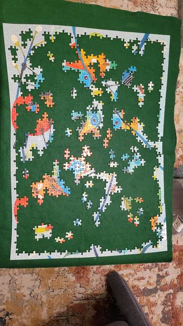 Photo from above of a partially finished jigsaw puzzle. Finished partial images of bright turquoise and teal birds, oranges, leaves, buds, and open flowers with white and light turquoise striping on the petals.