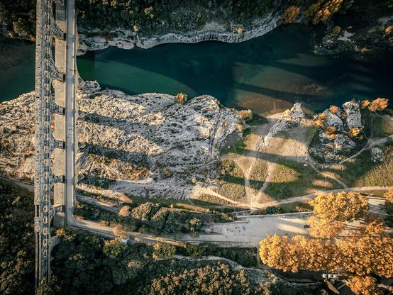 This 2000 years old roman aquaduct bridge stands in the middle of a hilly countryside in south of France above a river which can overflow quite fast.
It's the pinnacle of a former 50km long aquaduct. Taken with my DJI Mini 3 pro with autumn vibes.
<a href="https://en.wikipedia.org/wiki/Pont_du_Gard" rel="noreferrer nofollow">Wikipedia</a>.
