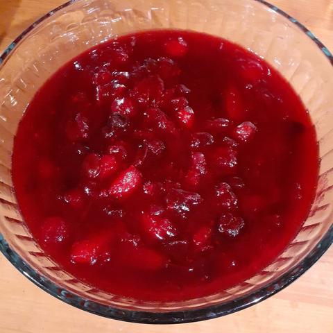 Chunky dark red cranberry sauce in a glass bowl on a wooden counter.