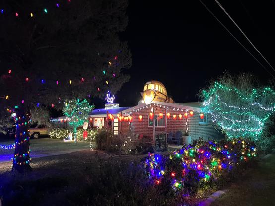House decorated with colorful Christmas lights at night, including illuminated trees and festive ornaments in the yard.