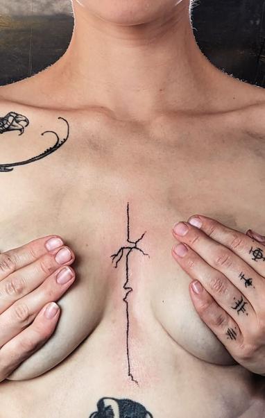 A person censors their breasts with their hands to show off a tattoo down their sternum. A centered line that wavers off and grows roots in various places, a simple organic freehanded sigil design.