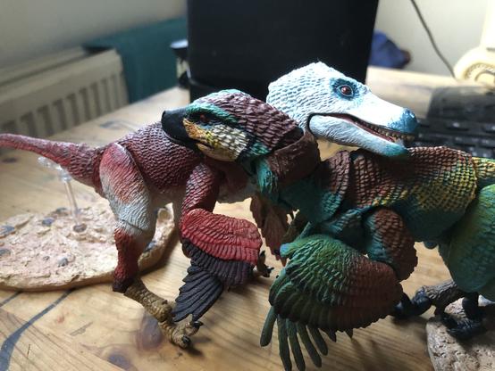 Two Beasts of the Mesozoic dinosaur toys posed giving each other a hug.