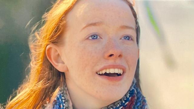 Close-up of a smiling girl with red hair and freckles, wearing a colorful scarf.