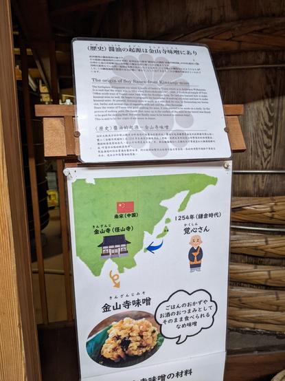 Printed sign with history of soy sauce in Japanese and English:

The origin of Soy Sauce from Kinzanji-miso

The birthplace of Japanese soy sauce is south of Osaka in Yuasa which is in Arida-gun Wakayama. It is said that the origin was in 1254 when Hottoukokushi (1207-1298) of Koukokuji temple of Yura (10km south-west of Yunsa) came back from the Southern Song. He had also learned how to make kinzanji miso as well. He began to propagate his knowledge of making soy sauce and how to make kinzanji miso. At present, kinzanji miso is made as a side dish for rice, by fermenting soy beans, rice, barley and several type of vegetable with salt and the other flavorings. Since the water of Yuasa was good making for miso, it was started to be made as a daily. In the process of making miso, the liquid that came up to the surface of the miso in the barrel was found to be good for cooking food. Soy sauce finally came to be brewed in various ways. This is said to be the origin of soy sauce in Japan.