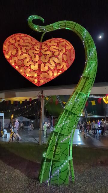 A green vine with a red / orange heart shaped fruit is lit up by LEDs.
