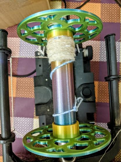 A 3d printed bobbin with a gradient of the colors yellow, green, blue, and purple