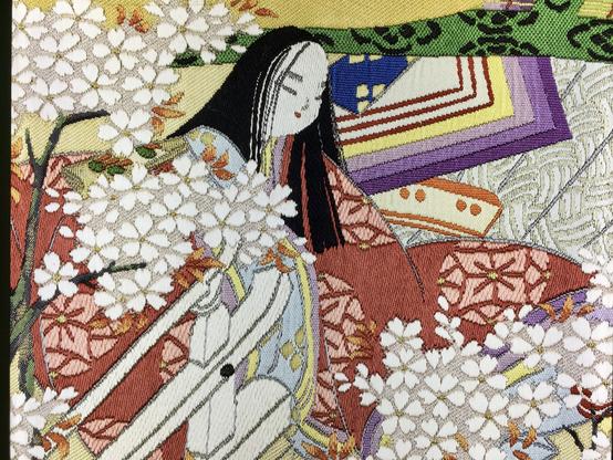 Détail du livre XLIV, La rivière aux bambous.
Gros plan sur l'une des dames de compagnie des princesses, à la longue chevelure brune, vêtue d'un kimono rouge à fleurs roses.
Assise, elle est en partie dissimulée derrière les branches d'un cerisier en fleur.