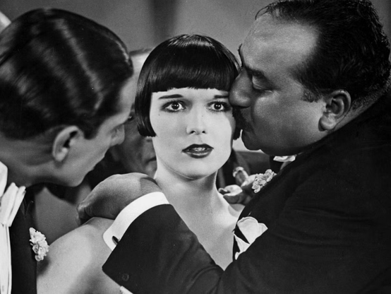 Louise Brooks in Pandora's Box.

She is looking straight ahead with a look of panic, concern, and maybe arousal? while one man drapes a hand over her shoulder and kisses her on the side of the head. Another man leans in hopefully. Another man is very close behind her, looking over her shoulder.