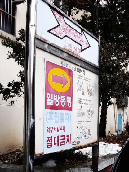 A large red right arrow is stuck on top of a sign. "One-way", "No reversing", and "No parking outside" are written in red.
