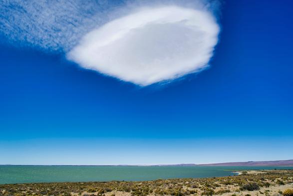 Big single white cloud in a deep blue sky above a lake surrounded by flat dry coastline.