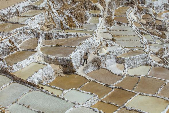 Woman walking between the salt water basins at the Pre Inca traditional salt mine (salinas) in Maras, Peru.