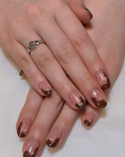 Chocolate brown swirls on nude nails with white stars and dots.