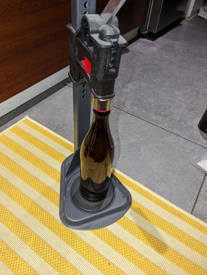 Une capsuleuse à colonne, posée à même le sol de la cuisine, prête à sertir une capsule couronne sur une bouteille.
