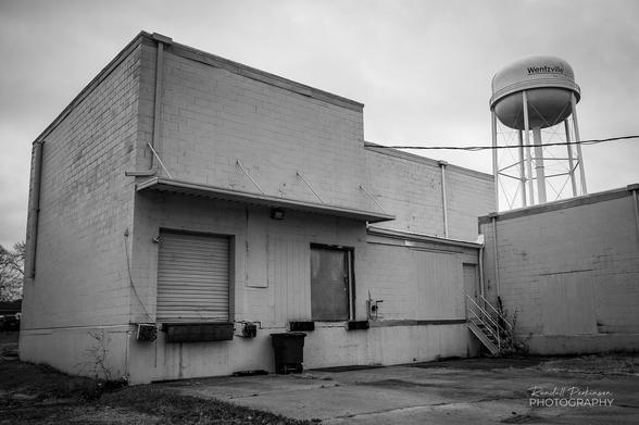 Back side of a vacant Industrial building with 2 loading dock doors. Wentzville water tower is in the background.