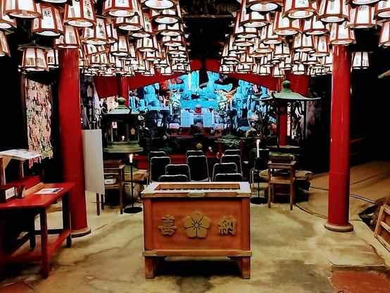 A small number of nearly lined up chairs sits in front of the altar, which is decorated with statues and is very colorful. The ceiling is illuminated with lots of canvas lanterns. The collection box sits in front of the chairs from my point of view. This temple doesn't appear to be that much different from other Buddhist ones. However, the fact that the walls are rough cave rock adds to the ambiance.
