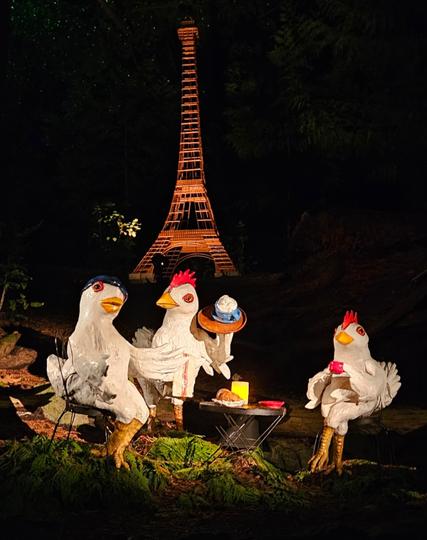Three large constructed hens drinking lattes in front of the Eiffel Tower at night.