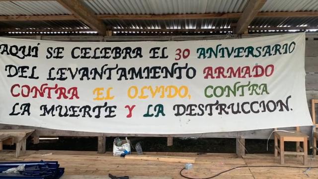 Banderole qui dit "Aquí se celebra el 30 aniversario del levantamiento armado contra el olvido, contra la muerte y la destrucción." Traduction : "Ici nous célébrons le 30e anniversaire du soulèvement armé contre l'oubli, la mort et la destruction."