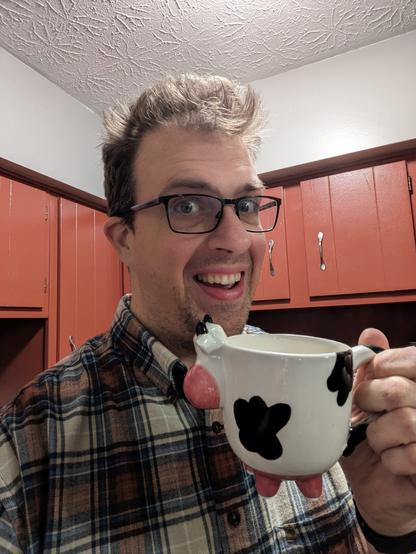 Me holding a mug in the shape of a cow. it rests on four feet which are the cow's udders.
