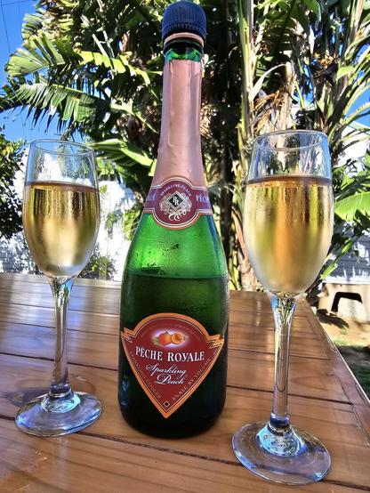 Bottle of peach flavoured sparkling wine, with a tall glass on each side of the bottle, each full of bubbly