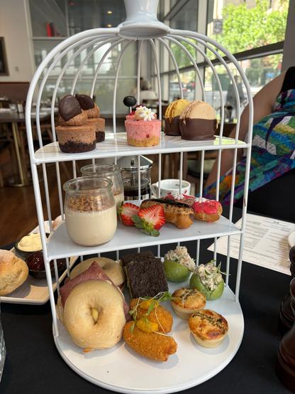 Cage containing three tiers of cakes and savoury treats.