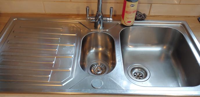 Photo of shiny clean stainless steel sink and draining drain, with a tub baking soda and a ball of steel wool