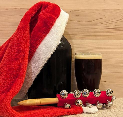 Glass of Jingle Hop Winter Red Ale from Wild Ride Brewing of Redmond, Oregon, poured from a growler; the growler itself has a Santa Claus hat draped over it, and there is a handheld jingle bell shaking instrument that looks a bit like a rattle in front of it.