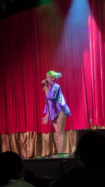 Sewer Rat Girl stands before a dark red curtain with no pants on at the opening of her show.

Things only got weirder from there.