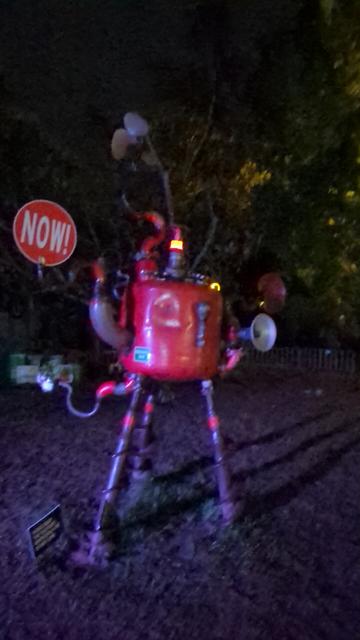 A red robot holding a "now" sign is frozen in place as it's legs are auger bits and have dug into the mud.