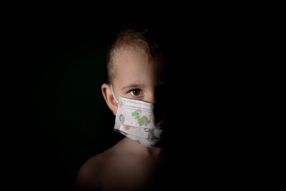 Boy, wearing a surgical mask for children, stares into the camera. He looks scared or intense... it's hard to tell.