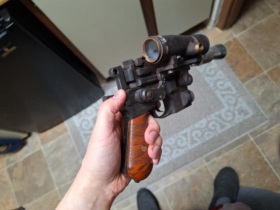 Rear isometric view of a DL44 blaster replica with a closer look at the painted woodgrain handgrip and the back end of the large offset scope
