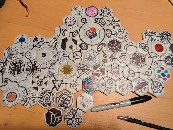 Small hexagonal tiles, each decorated with sharpie in abstract designs. Each tile has three lines connecting it to other tiles on alternating faces of the hexagon.