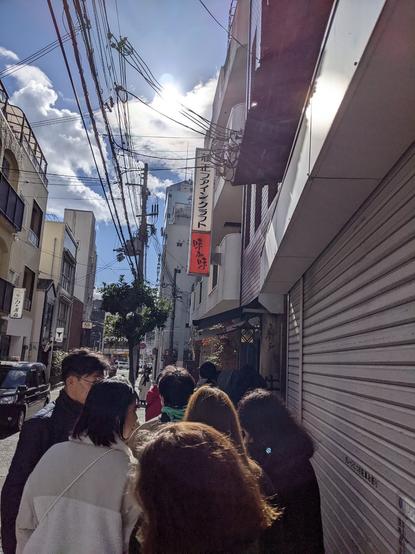 Line outside Kobe Beef Hiroshige on a street pavement - about 8 people in front with steel shutter to the right