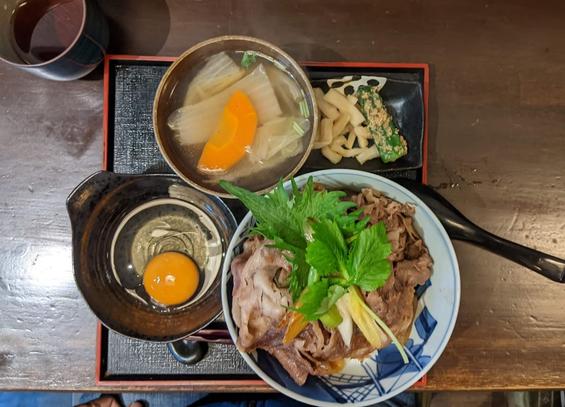 Top view of a square tray with a bowl of beef over rice and a bowl with egg and a bowl of soup and small dish with pickles (radish and nakazuke okra)