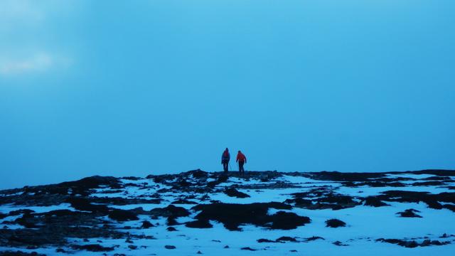 Two friends, on the horizon, walking up the snow covered hill.