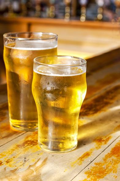 Two light golden beers on a wooden bar.
One pint and one half a pint