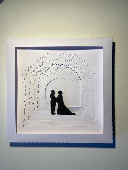 Shadow box art showing a couple on their wedding day in silhouette facing each other. The couple are cut from black paper, the rest is in white.