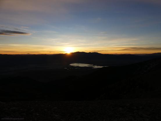 Sunrise over Springs Valley where Yelland Dry Lake isn't very dry, seen from the ridge of the Schell Creek Range in High Schells Wilderness, Humboldt-Toiyabe National Forest, Nevada.

Yellow light bursting over dark mountains reflect from a body of water in a dark valley. The sky shades to blue toward the top. There are some clouds, mostly down near the peaks.